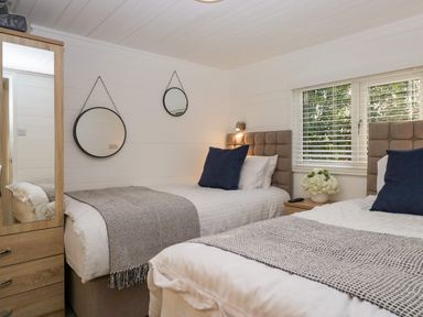 A bedroom with two single beds a bedside table with flowers and a mirror on the wall at Esk Pike 9 Skiptory Howe White Cross Bay near Windermere