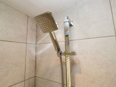 A close up of a square handheld shower head mounted on a rail in a tiled shower at Esk Pike 9 Skiptory Howe White Cross Bay near Windermere