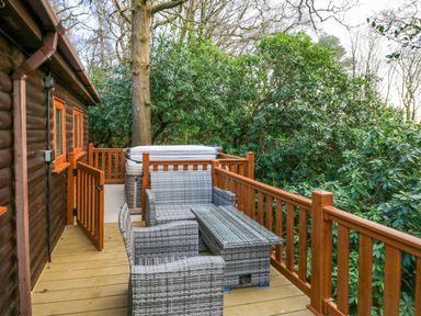 An outdoor deck with wicker seating furniture and a hot tub surrounded by wooden railings at Esk Pike 9 Skiptory Howe White Cross Bay near Windermere