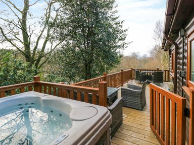 An outdoor wooden deck with a hot tub and patio furniture surrounded by trees at Esk Pike 9 Skiptory Howe White Cross Bay near Windermere
