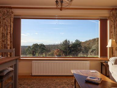 A living room with a large window overlooking trees and countryside at Sherway Dairy in Clyst Hydon near Bradninch