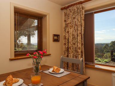A dining table with croissants and orange juice near windows with floral curtains and blinds at Sherway Dairy in Clyst Hydon near Bradninch