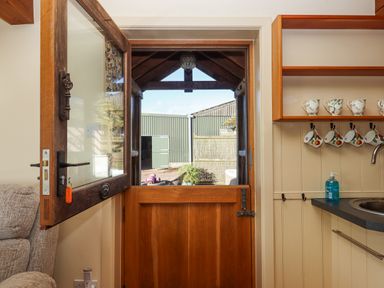 An open wooden stable door leading outside with kitchen countertop and mugs hanging on hooks inside at Sherway Dairy in Clyst Hydon near Bradninch
