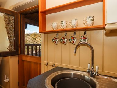 A kitchen sink area with four mugs hanging on hooks under a wooden shelf with four matching cups at Sherway Dairy in Clyst Hydon near Bradninch