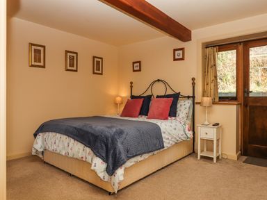A bedroom with a bed with red and blue pillows nightstands with lamps framed pictures on the walls and a wooden door at Sherway Dairy in Clyst Hydon near Bradninch