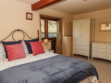 A bedroom with a bed with pillows and a blanket a wardrobe a dresser a lamp and a window at Sherway Dairy in Clyst Hydon near Bradninch