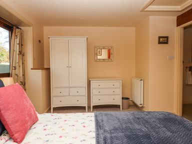 A bedroom with a bed with floral bedspread and pillows a white wardrobe a white chest of drawers a small mirror on the wall and a radiator at Sherway Dairy in Clyst Hydon near Bradninch