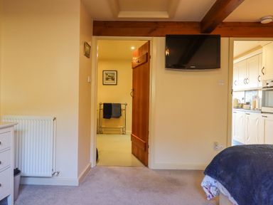 A bedroom with a bed partly visible a wall mounted TV an open door showing a hallway and a view into a kitchen at Sherway Dairy in Clyst Hydon near Bradninch