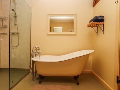 A bathroom with a clawfoot bathtub a shower area with glass partition a rectangular mirror and a wall shelf with folded towels at Sherway Dairy in Clyst Hydon near Bradninch