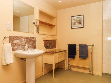 A bathroom with a sink and mirror a wooden cabinet a towel rack with dark towels and a framed picture on the wall at Sherway Dairy in Clyst Hydon near Bradninch
