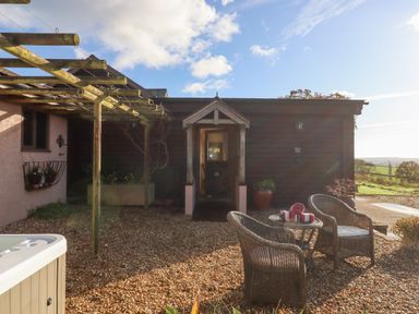 A gravel patio with two wicker chairs and a table with towels in front of a wooden building at Sherway Dairy Clyst Hydon near Bradninch