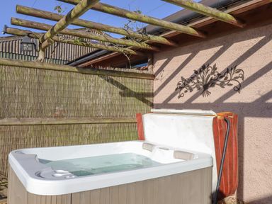 An outdoor hot tub with a partially open cover under a wooden pergola at Sherway Dairy in Clyst Hydon near Bradninch