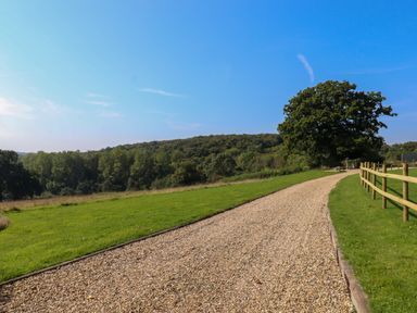 A gravel pathway bordered by grass and a wooden fence with trees and hills in the background at Sherway Dairy in Clyst Hydon near Bradninch