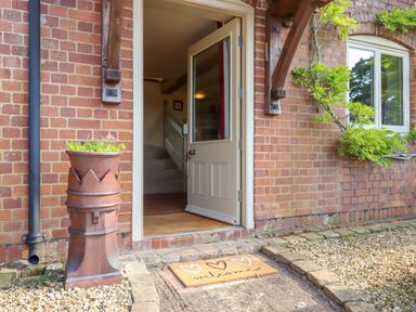 An open front door with a welcome mat and a plant pot outside a brick house at Sherway Shippen in Clyst Hydon near Bradninch