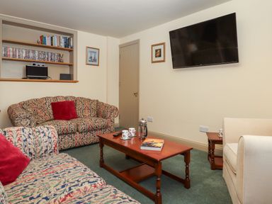 A sitting room with patterned sofas a wooden coffee table a wall-mounted television and shelves with books and DVDs at Sherway Shippen in Clyst Hydon near Bradninch