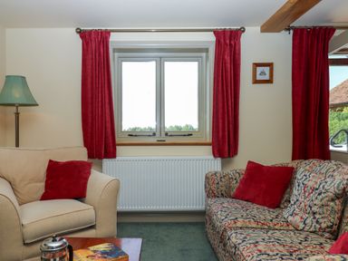 A living room with beige armchair red cushions patterned sofa red curtains and a window at Sherway Shippen in Clyst Hydon near Bradninch