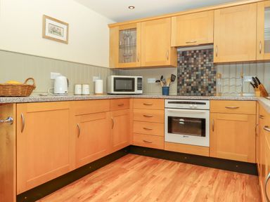 A kitchen with wooden cabinets a microwave a white oven cooking utensils a kettle and a basket of fruit at Sherway Shippen in Clyst Hydon near Bradninch