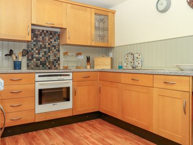 A kitchen with wooden cabinets an oven countertop with kitchen utensils a bread box and a sink at Sherway Shippen in Clyst Hydon near Bradninch
