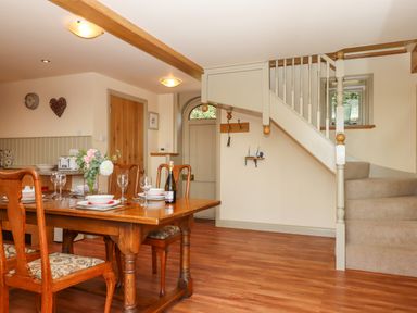 A dining area with a wooden table, chairs, staircase, and a door at Sherway Shippen in Clyst Hydon near Bradninch