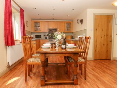 A dining area with a wooden table and six chairs set with plates glasses and a bottle in a kitchen at Sherway Shippen in Clyst Hydon near Bradninch