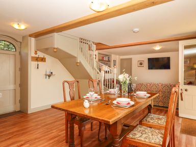 A dining area with a wooden table set for four and chairs near a staircase and a living room at Sherway Shippen in Clyst Hydon near Bradninch