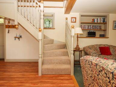A staircase with carpeted steps and white balusters next to a seating area with patterned sofas and a side table with a lamp at Sherway Shippen in Clyst Hydon near Bradninch