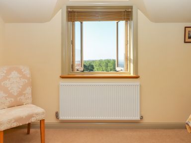 A room with an open window showing trees outside a radiator under the window and a beige patterned chair Sherway Shippen Clyst Hydon near Bradninch