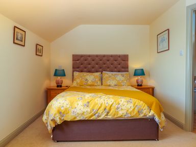 A bedroom with a bed with yellow floral bedding two bedside tables with lamps and framed pictures on the walls at Sherway Shippen in Clyst Hydon near Bradninch
