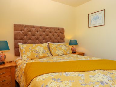 A bedroom with a bed with floral bedding and a brown tufted headboard with two bedside tables and blue lamps at Sherway Shippen in Clyst Hydon near Bradninch