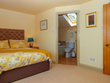 A bedroom with a bed and bedside table next to an open door showing a bathroom at Sherway Shippen in Clyst Hydon near Bradninch