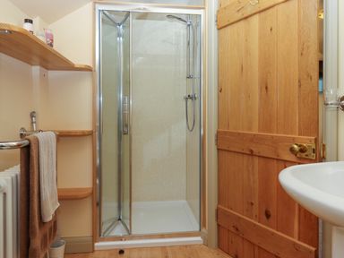A bathroom with a wooden door a glass shower enclosure a sink wooden shelves with bottles and towels at Sherway Shippen in Clyst Hydon near Bradninch