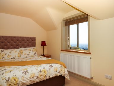 A bedroom with a bed featuring floral bedding and a yellow throw next to a window with wooden blinds at Sherway Shippen in Clyst Hydon near Bradninch