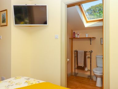 A bedroom with a wall-mounted television and an open door showing a bathroom with a toilet towel rack and a skylight window at Sherway Shippen in Clyst Hydon near Bradninch