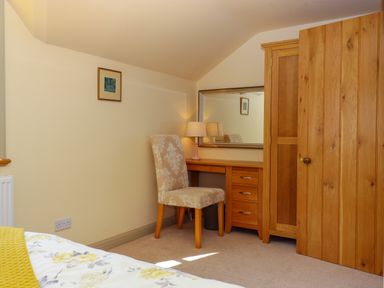 A bedroom with a wooden desk with drawers a chair a lamp a mirror a wooden door and a bed with floral bedding at Sherway Shippen in Clyst Hydon near Bradninch