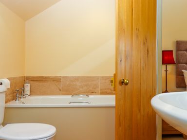 A bathroom with a bathtub toilet and a wooden door partially open showing a bedroom with a red lamp at Sherway Shippen in Clyst Hydon near Bradninch