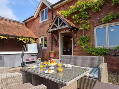 An outdoor patio area with a wicker dining set with orange juice and croissants in front of a brick house at Sherway Shippen in Clyst Hydon near Bradninch
