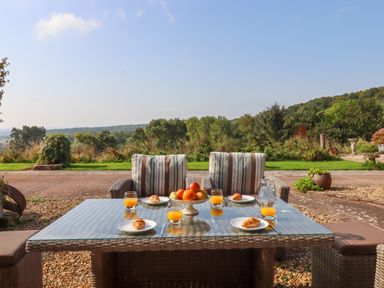 An outdoor dining table with croissants orange juice and fruit bowl in a garden at Sherway Shippen in Clyst Hydon near Bradninch