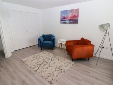 A room with a blue and orange armchair a white side table a floor lamp a painting on the wall and a rug on the floor at 69 Ffordd Y Meillion in Llanelli