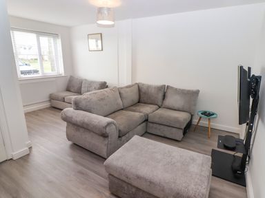 A living room with grey sofas a window small round table and a wall mounted television at 69 Ffordd Y Meillion in Llanelli
