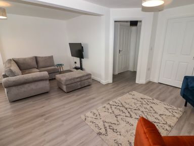 A living room with a grey sofa and ottoman a wall mounted television a patterned rug and white doors at 69 Ffordd Y Meillion in Llanelli