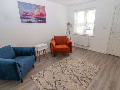 A living room with a blue sofa a red armchair a white side table a floor lamp a patterned rug and a colorful painting at 69 Ffordd Y Meillion Llanelli