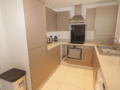 A kitchen with brown cabinets a stainless steel oven a stovetop a sink and a silver trash bin at 69 Ffordd Y Meillion in Llanelli