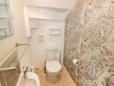 A small bathroom with a toilet, sink, mirror, and patterned wallpaper at 69 Ffordd Y Meillion in Llanelli
