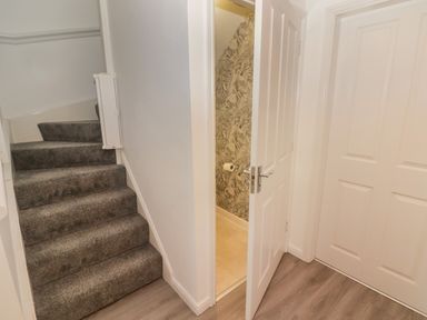 A hallway with carpeted stairs and two white doors one partially open showing a wall with patterned wallpaper at 69 Ffordd Y Meillion in Llanelli