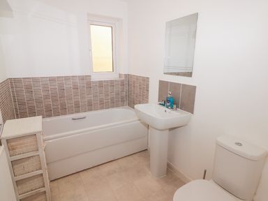 A bathroom with a bathtub a pedestal sink a toilet a window and a small storage unit at 69 Ffordd Y Meillion in Llanelli