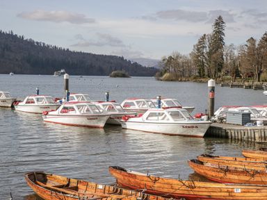 Boats moored at a dock with trees and mountains in the background at Claife Flights Bowness-On-Windermere