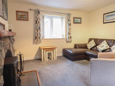 A living room with a stone fireplace nested tables a window with curtains a brown leather sofa and framed pictures on the walls at Ysgubor Newydd Parc Isaf in Dyffryn Ardudwy