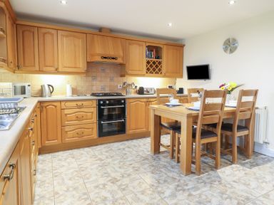 A kitchen with wooden cabinets and a dining table set with plates glasses and flowers at Ysgubor Newydd Parc Isaf in Dyffryn Ardudwy