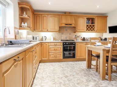 A kitchen with wooden cabinets tiled floor and dining table with chairs at Ysgubor Newydd Parc Isaf in Dyffryn Ardudwy