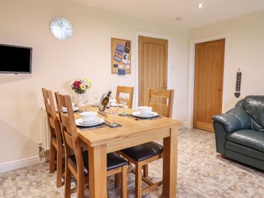 A dining area with a wooden table set with bowls, plates, and glasses near two wooden doors and a green armchair at Ysgubor Newydd Parc Isaf Dyffryn Ardudwy
